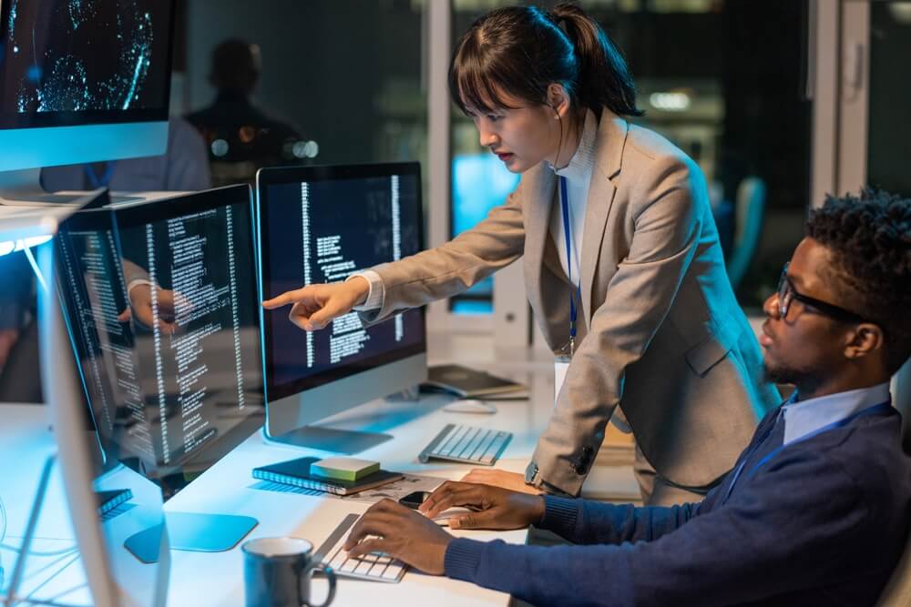 female IT pointing at data on computer screen while discussing with male colleague