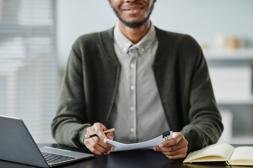 man holding a paper and pen in front of a laptop