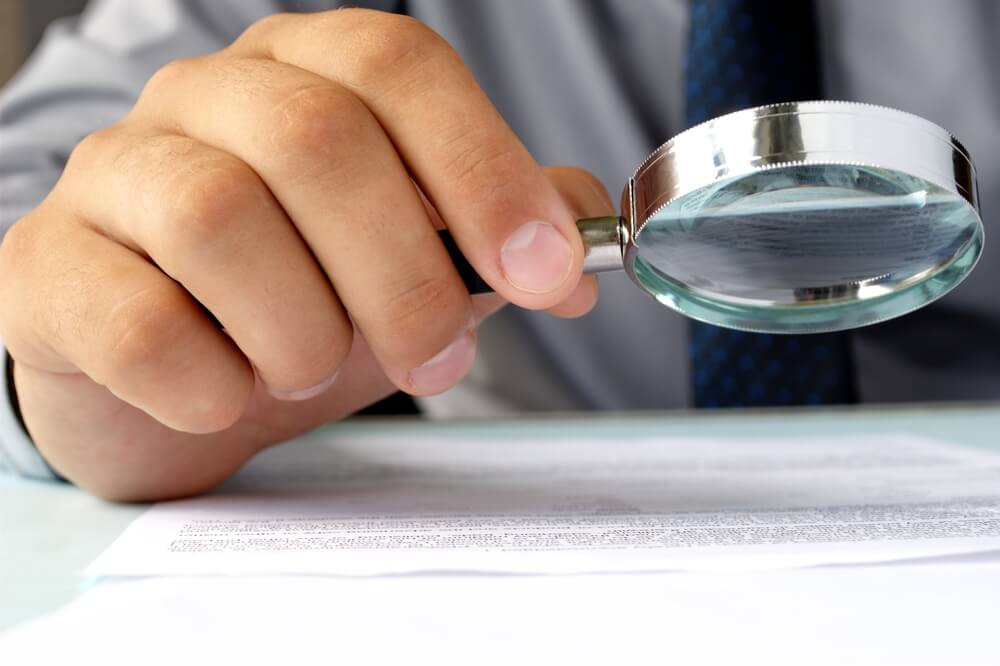 hand of a man holding magnifying glass on paper